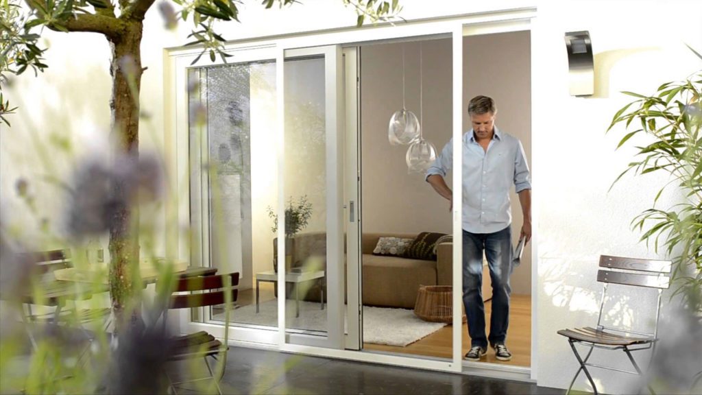 modern home interior with large glass sliding doors opening to a patio area with plants and outdoor furniture. A man is standing inside the open doorway